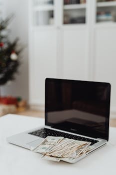 Laptop with dollar bills on desk, capturing a finance and home office theme.