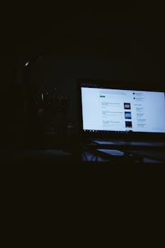 Low light ambiance of a laptop screen glowing in a dark, quiet workspace.